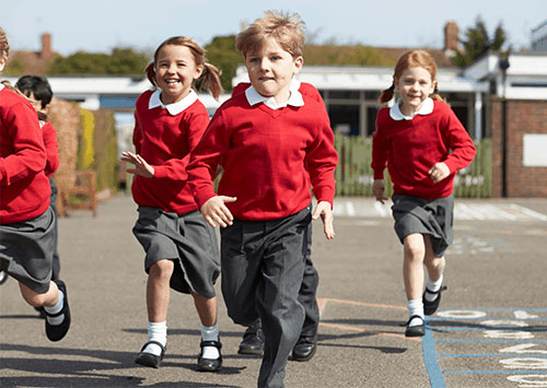 Young primary school children wearing red uniform running through the playground on a sunny day.